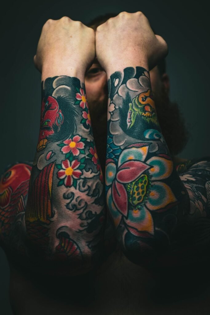 Zwei Unterarme voller bunter Old-School-Tattoos mit Blumen und Koi